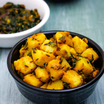 Jeera aloo served in a bowl with methi bhaji and dal in the back.