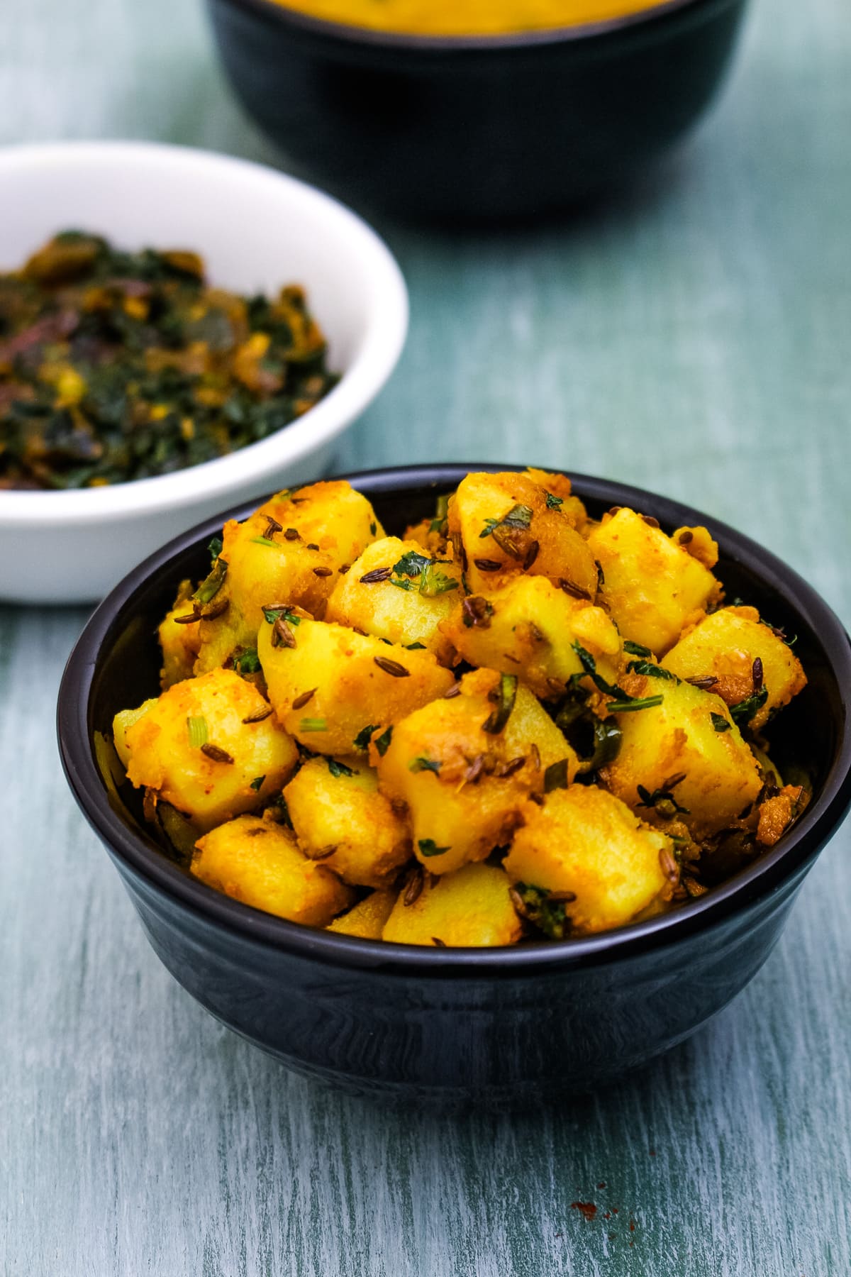 Jeera aloo served in a bowl with methi bhaji and dal in the back.