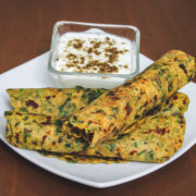 3 methi paratha roll served with a bowl of yogurt.