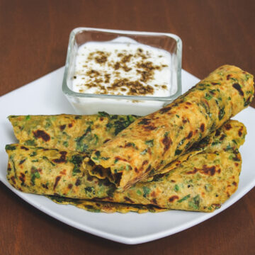 3 methi paratha roll served with a bowl of yogurt.