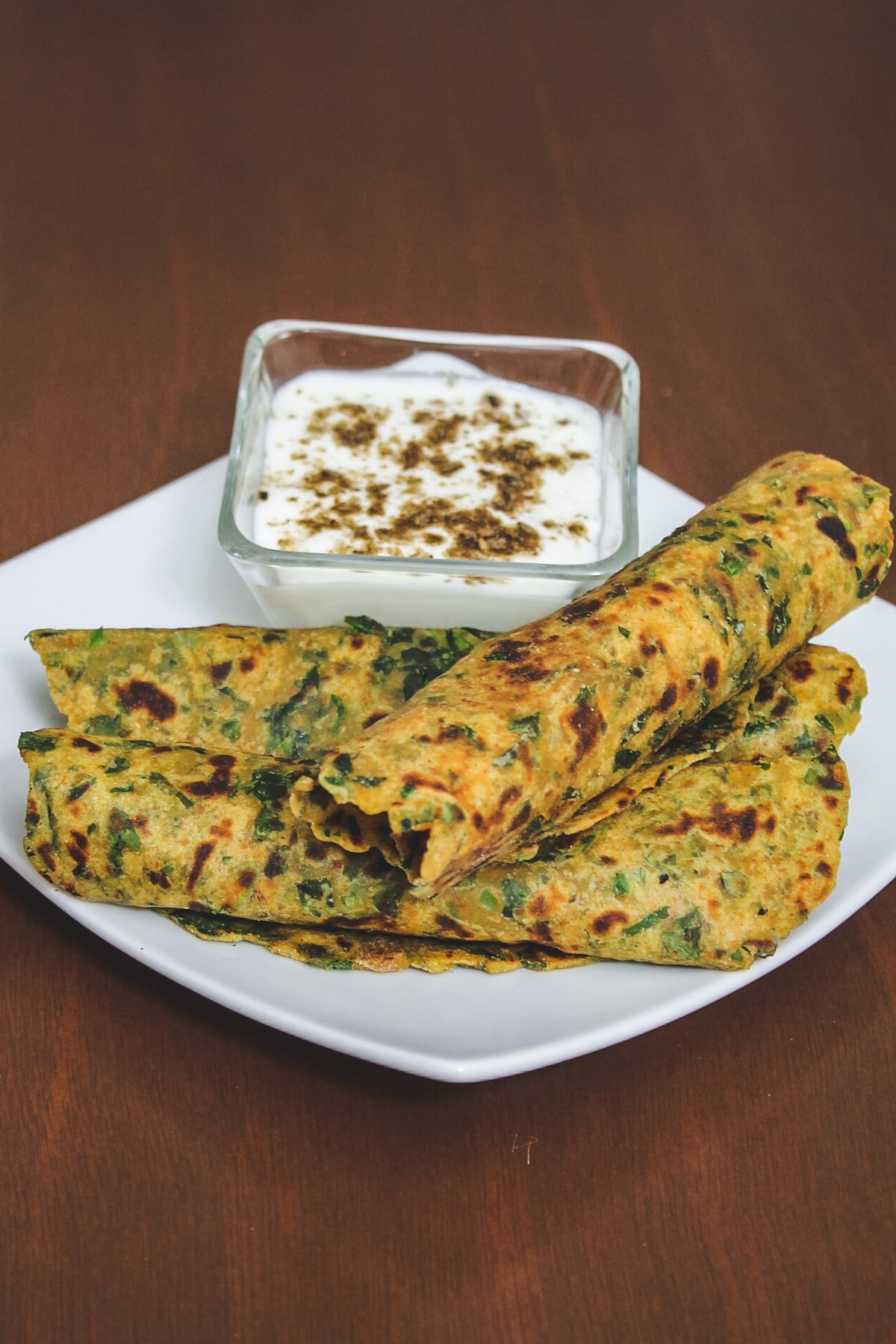 3 methi paratha roll served with a bowl of yogurt.