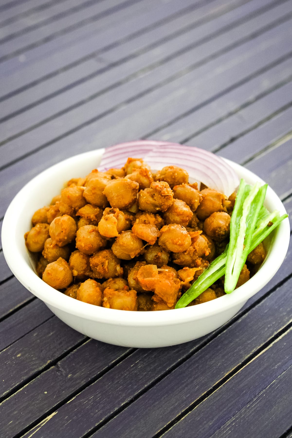 Pindi chole served in a bowl with garnish of green chili and sliced onions.