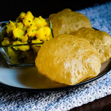 Close up of poori served with batata sabzi and chickenkari napkin underneath.