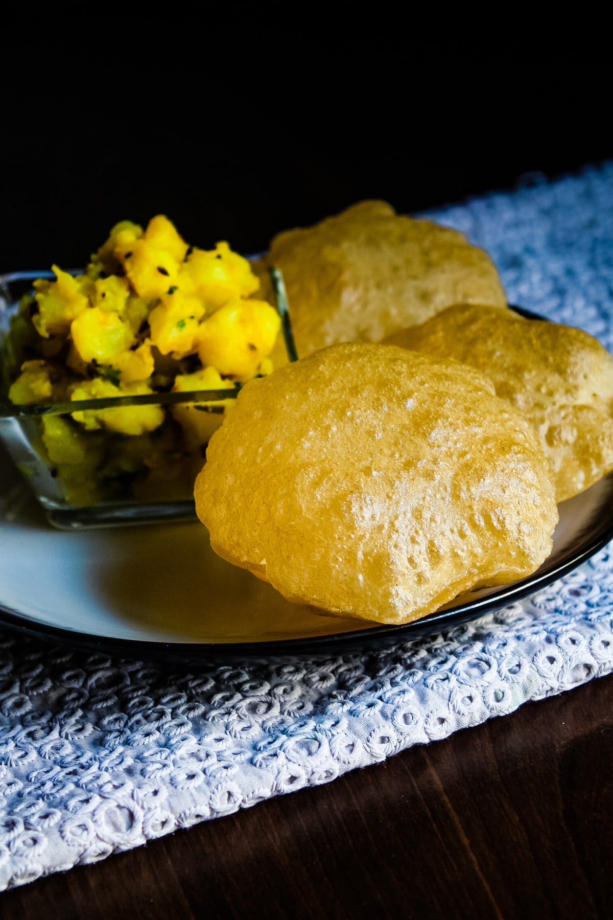 Close up of poori served with batata sabzi and chickenkari napkin underneath.
