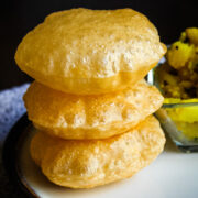 stack of 3 pooris in a plate with batata bhaji in the back.