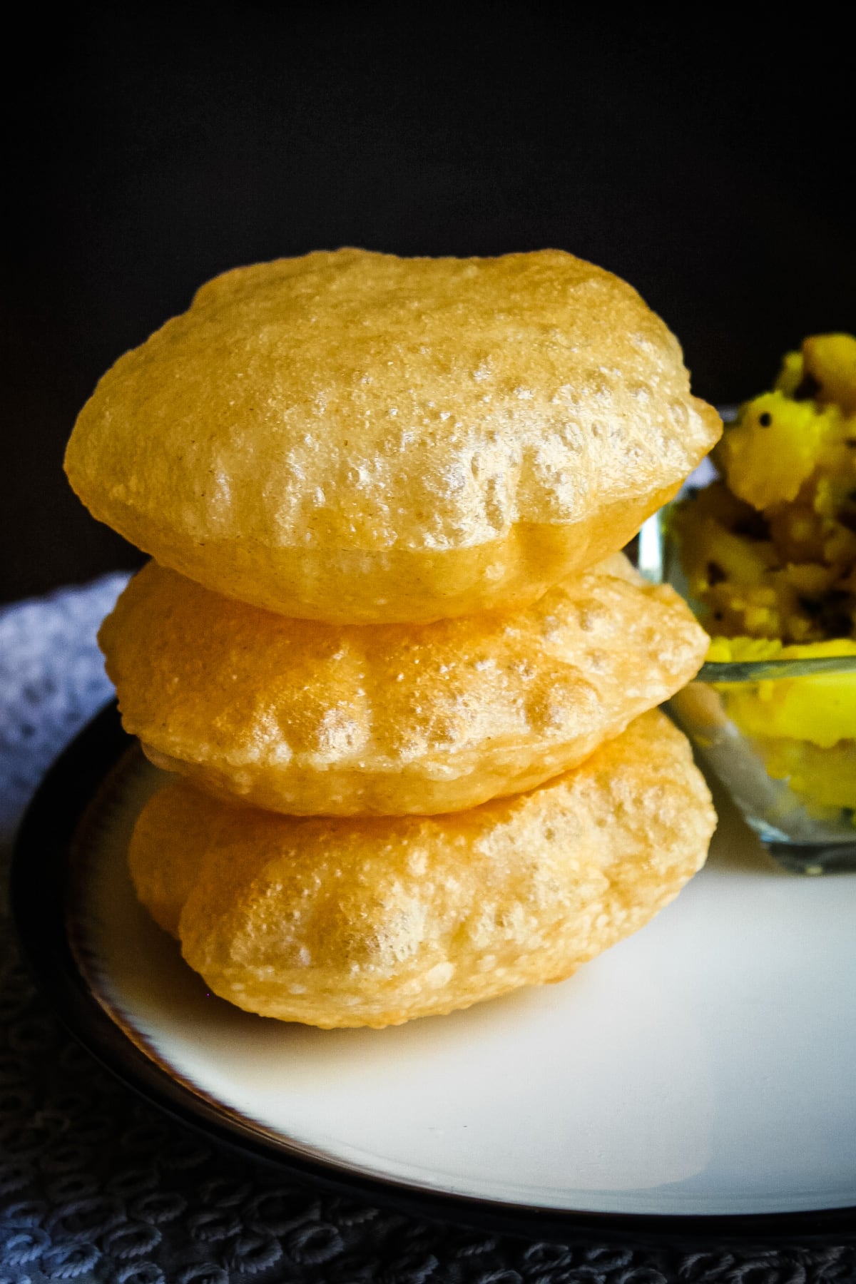 stack of 3 pooris in a plate with batata bhaji in the back.