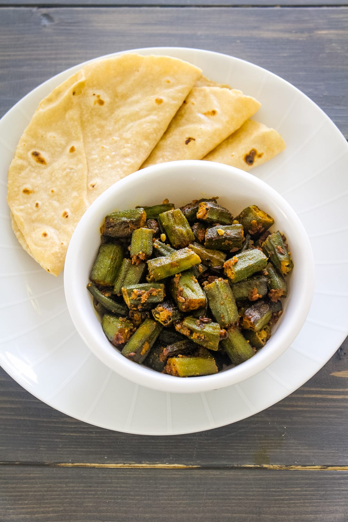 Achari bhindi served with a bowl with 3 phulka roti.