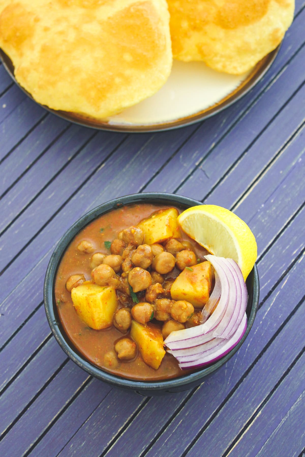 Aloo chole served in a bowl with garnish of onions and lemon wedge, bhatura on the side.