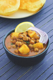 Close up of aloo chana in a black bowl with sliced onions and lemon wedge.