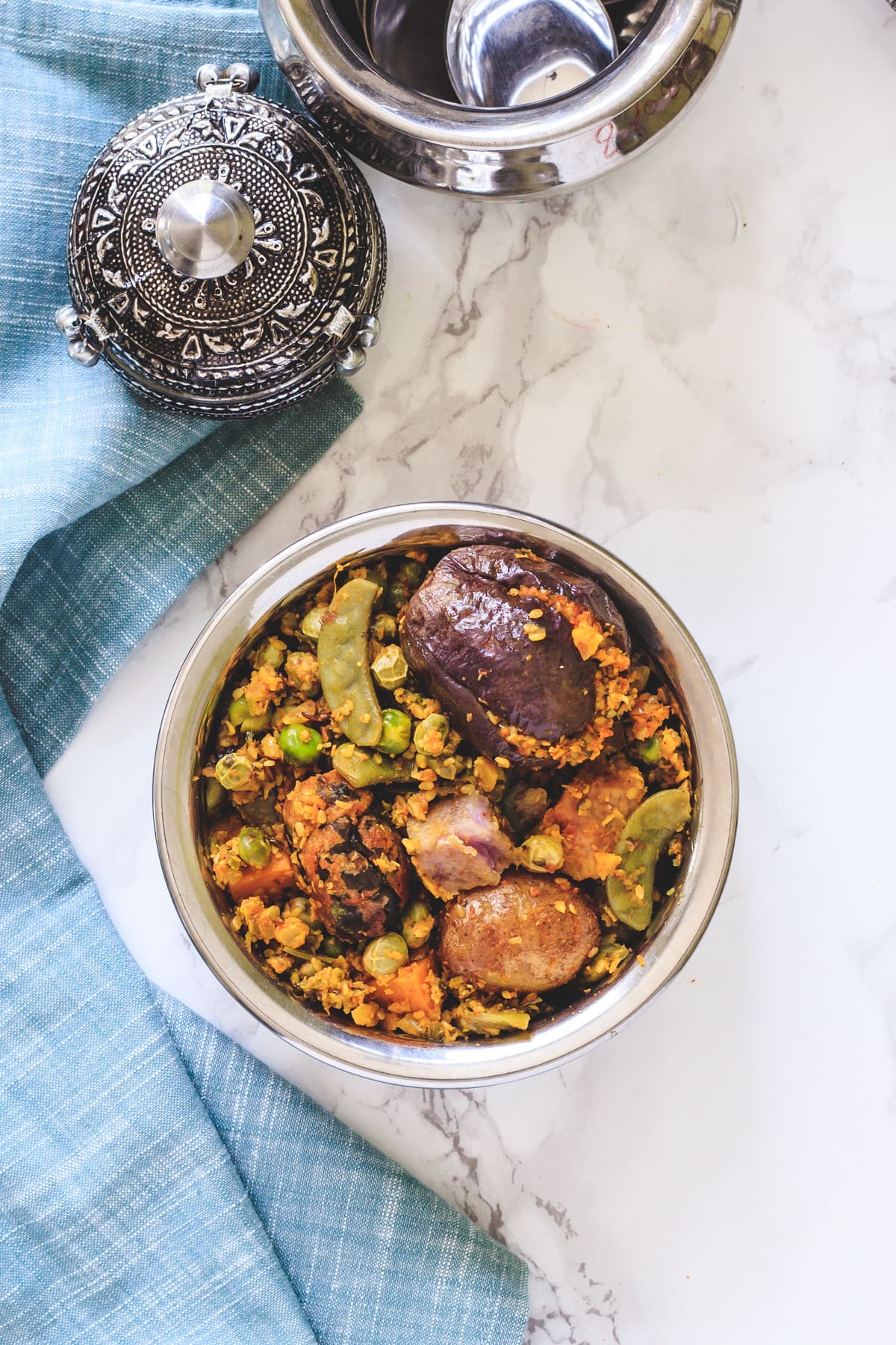 Top view of undhiyu in steel bowl with napkin on side.