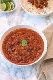 Kala chana served in a white bowl with a garnish of cilantro leaf with napkin and limes, rice on side.