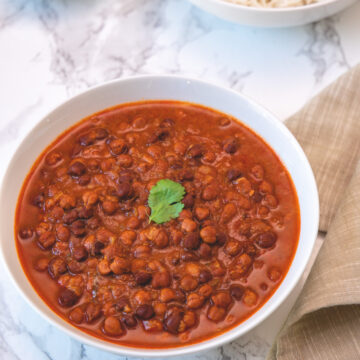 Kala chana served in a white bowl with a garnish of cilantro leaf with napkin and limes, rice on side.