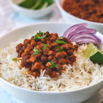 Kala chana masala served over a bowl of rice with side of sliced onions and lime wedge.