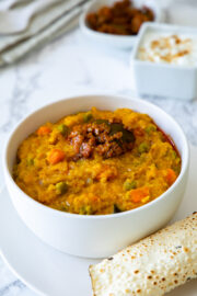 Quinoa khichdi topped with pickle served with a bowl yogurt & papad.