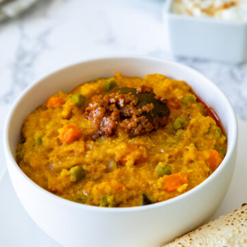 Quinoa khichdi topped with pickle served with a bowl yogurt & papad.