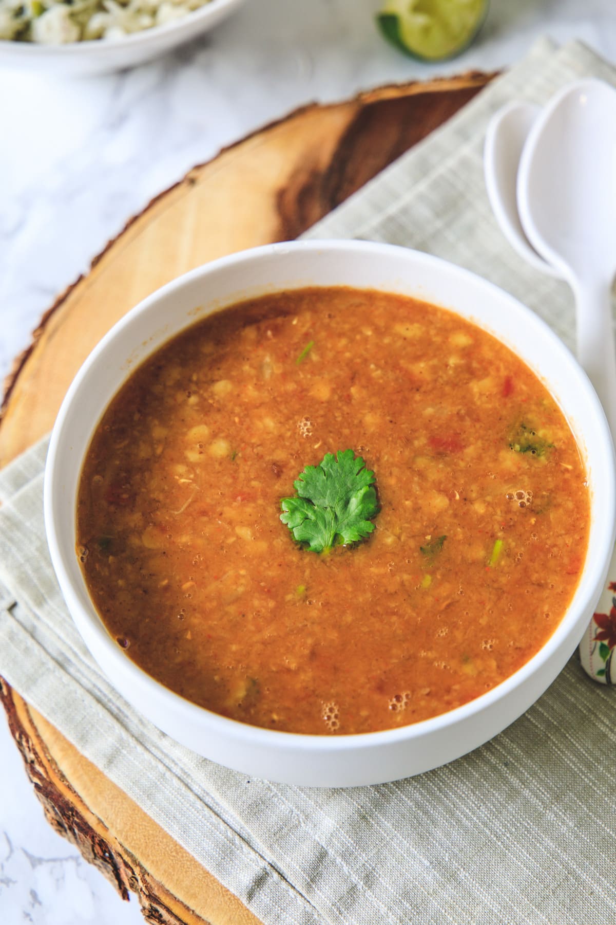 Toor dal garnished with cilantro leaf in a bowl with napkin underneath and 2 spoons on side.