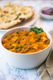 Matar paneer garnished with cilantro, napkin on the side, naan & onion served in the back.
