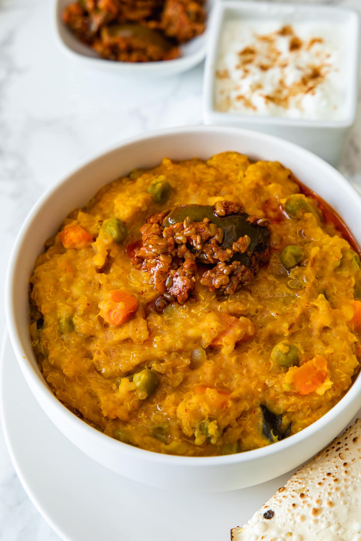 Close up of quinoa khichdi topped with pickle, yogurt and more pickle in the back.