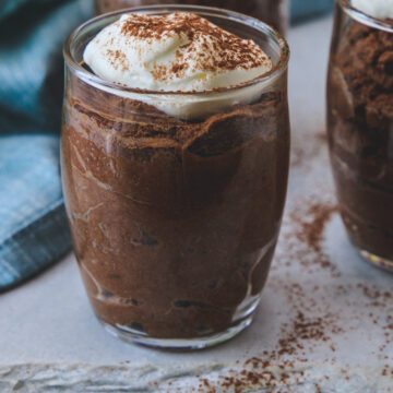 Individual serving glass of eggless chocolate mousse garnished with whipped cream and cocoa powder.