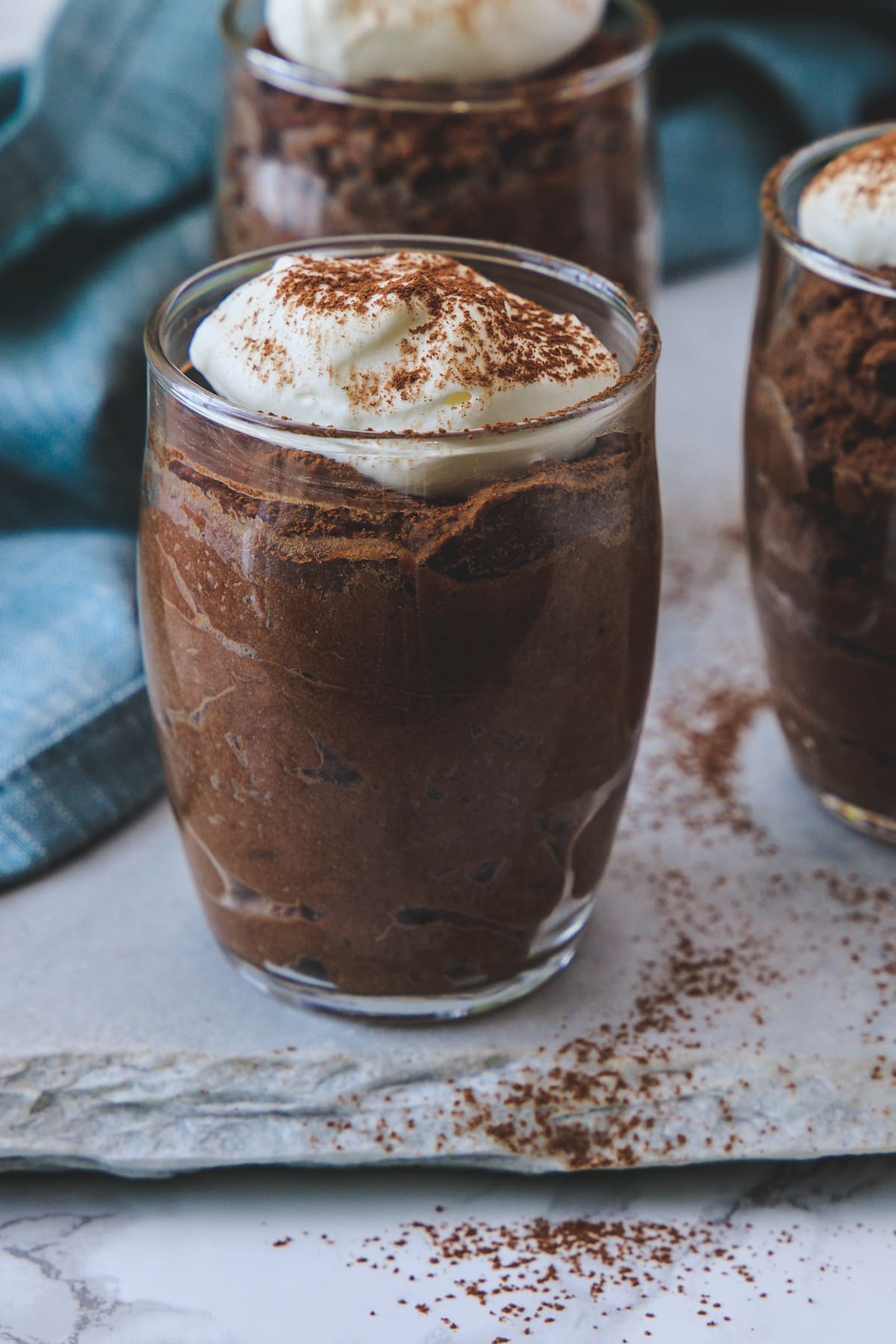 Individual serving glass of eggless chocolate mousse garnished with whipped cream and cocoa powder.