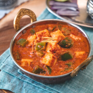 Kadai paneer served in a serving wok with onions, lime on side with napkin underneath.