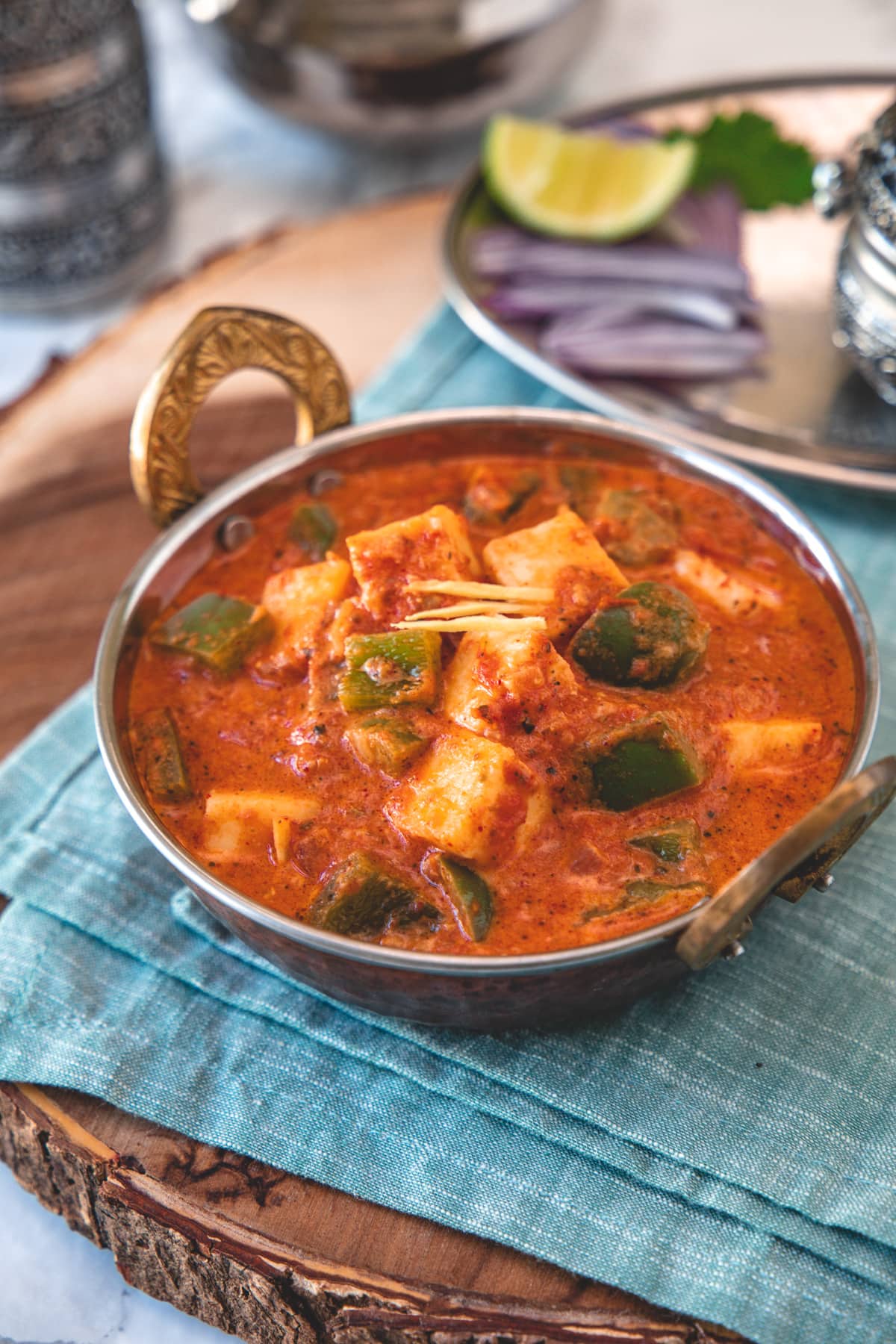 Kadai paneer served in a serving wok with onions, lime on side with napkin underneath.