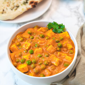 A bowl of matar paneer garnished with cilantro, naan and onions in the back.