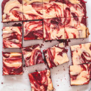 Top view of red velvet cheesecake swirl brownie pieces on a parchment paper with knife on the side.