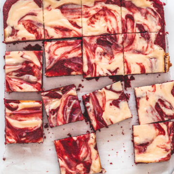 Top view of red velvet cheesecake swirl brownie pieces on a parchment paper with knife on the side.