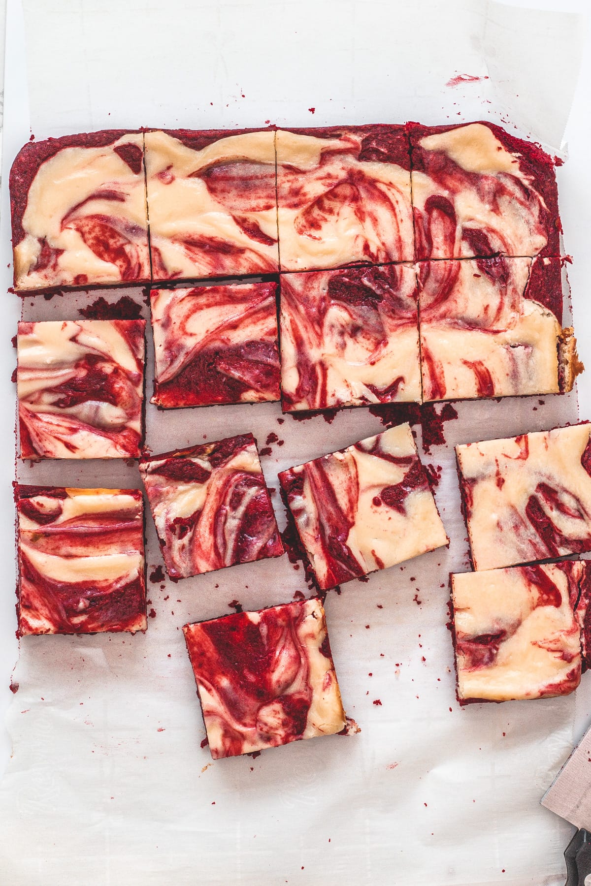Top view of red velvet cheesecake swirl brownie pieces on a parchment paper with knife on the side.
