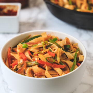 Schezwan noodles served in a bowl with more noodles in the pan in the back.