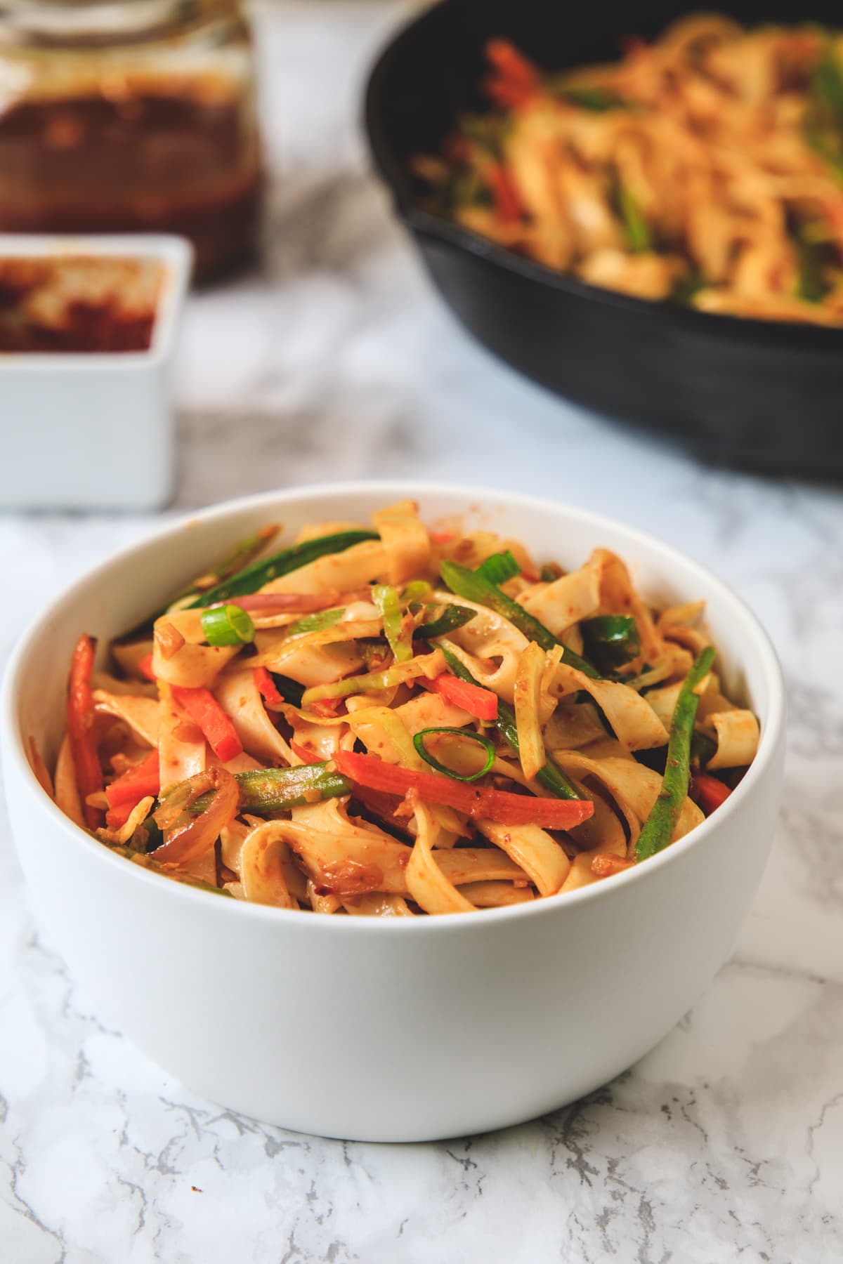 Schezwan noodles served in a bowl with more noodles in the pan in the back.