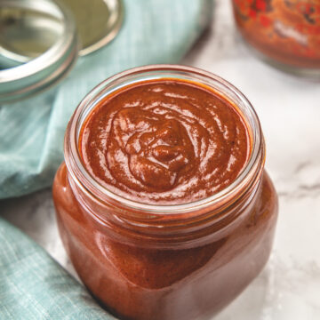 Enchilada sauce in a glass jar with napkin on side.