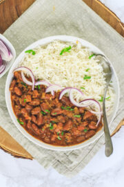 Rajma chawal in a plate with a spoon, garnished with cilantro and served with sliced onions.