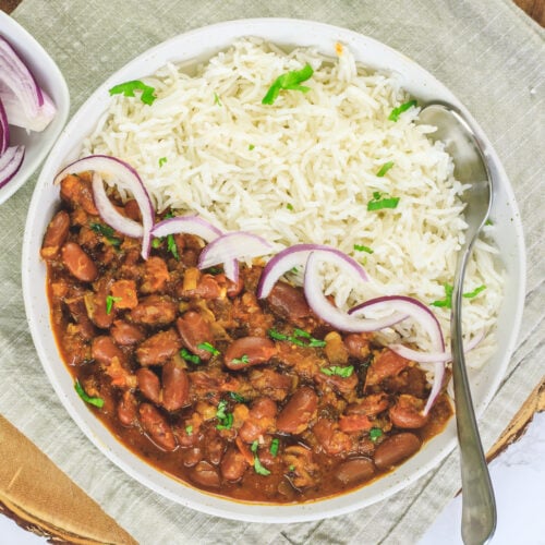 Rajma chawal in a plate with a spoon, garnished with cilantro and served with sliced onions.