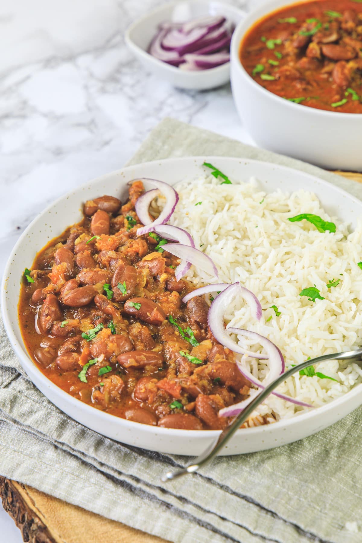 Rajma masala served with rice and sliced onions with a spoon in the plate.