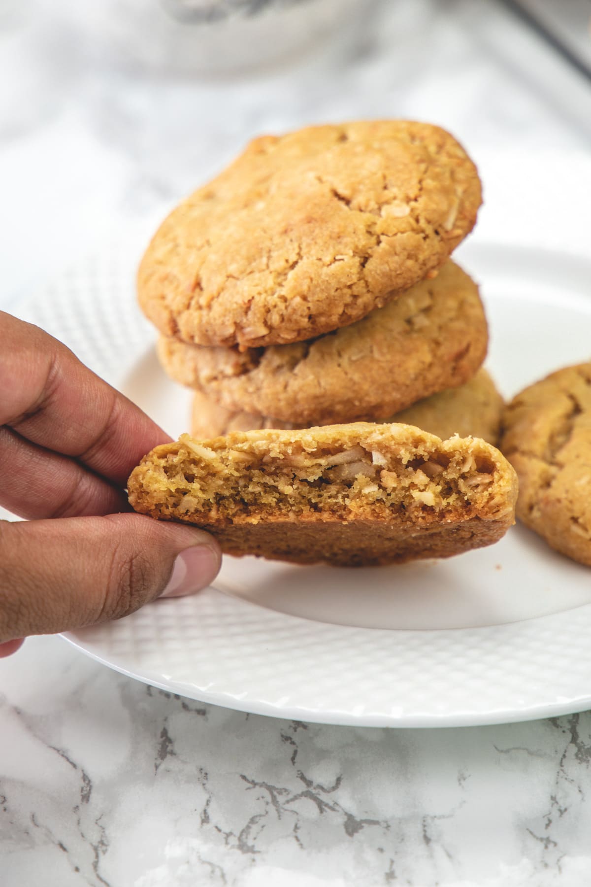 halved eggless coconut cookie to show inside texture with a stack of cookies behind.