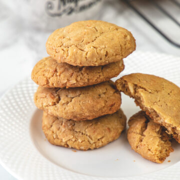 Stack of 4 eggless coconut cookies in a plate with one cookie broken into half on the side.