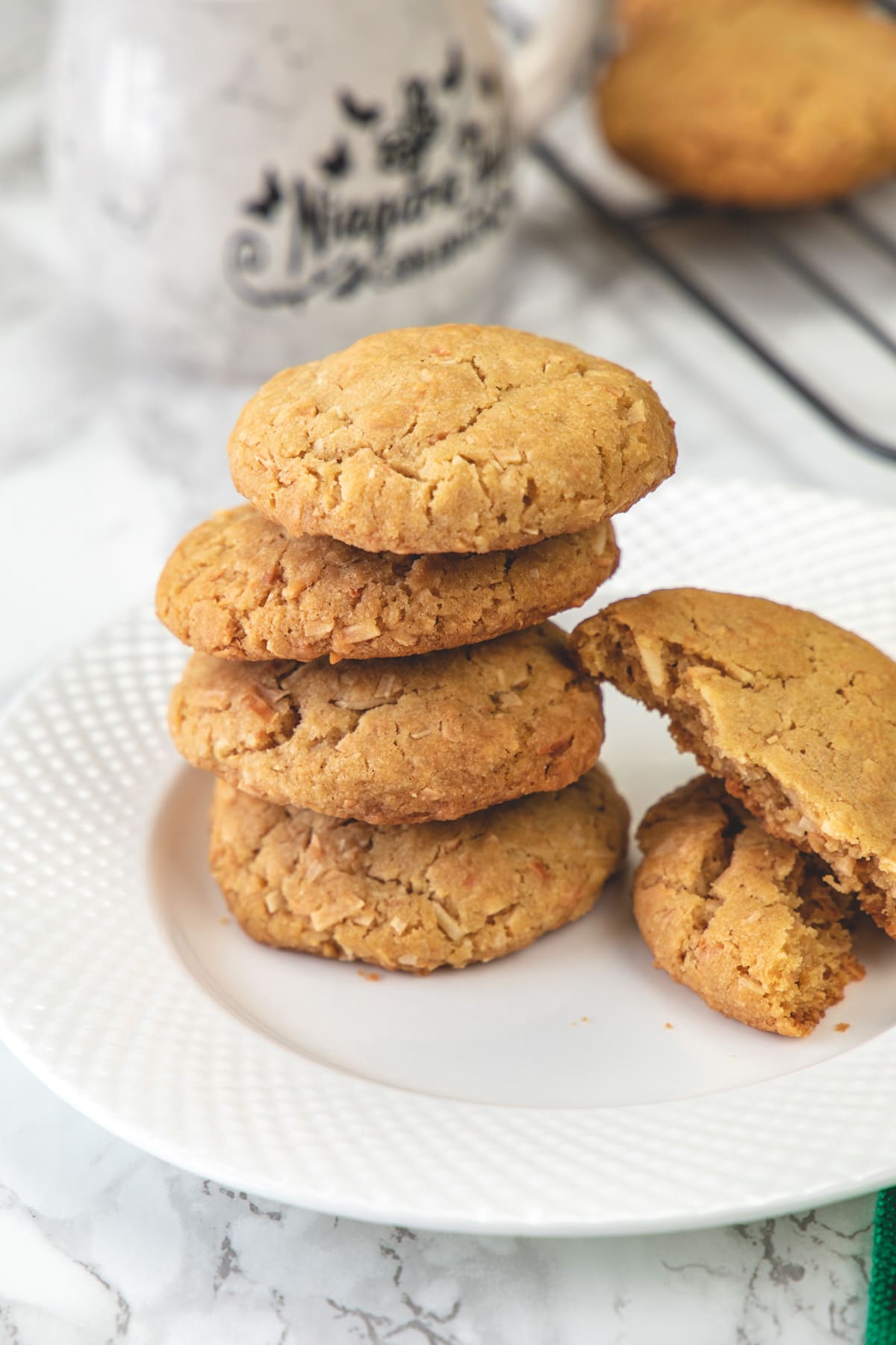 Stack of 4 eggless coconut cookies in a plate with one cookie broken into half on the side.