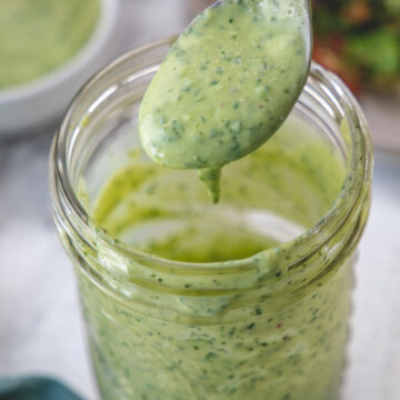 A spoonful of avocado lime dressing drizzling back into the mason jar to show consistency.