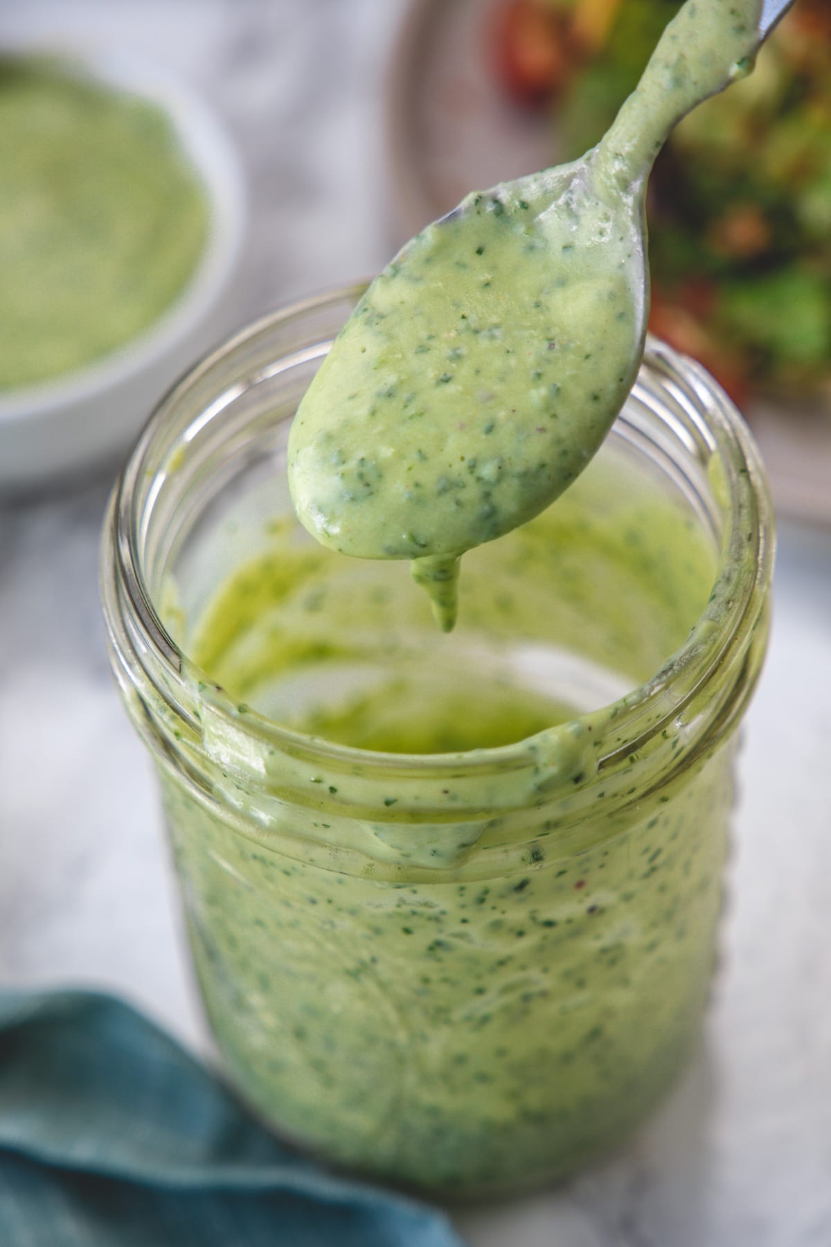 A spoonful of avocado lime dressing drizzling back into the mason jar to show consistency.