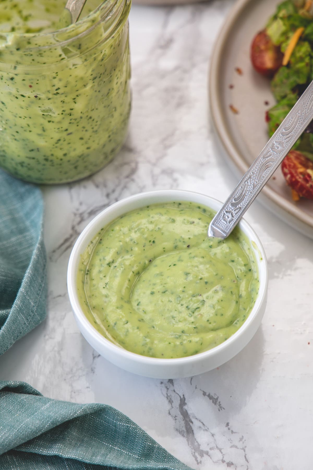 A white bowl of avocado lime salad dressing with salad plate and more dressing in the back.