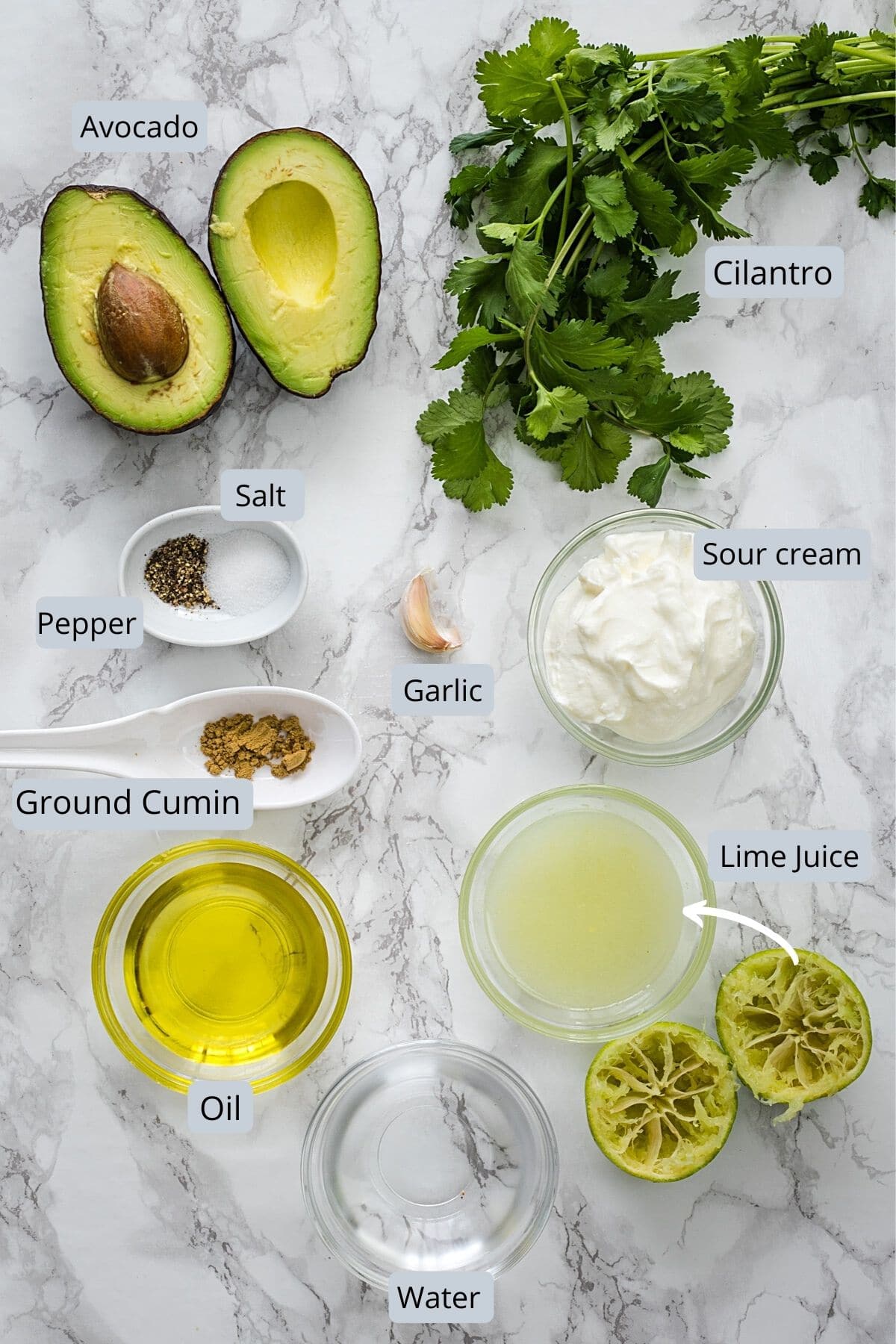 Ingredients used in avocado lime dressing in individual bowls on marble surface.