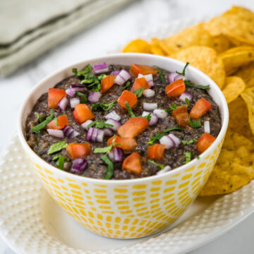 Black bean dip in a bowl garnished with onion, tomato, cilantro and served with tortilla chips.