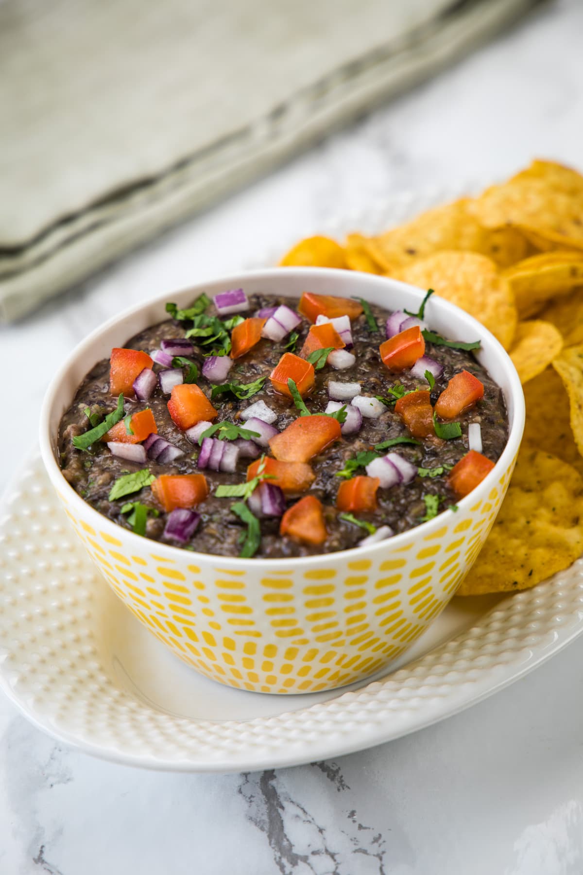 Black bean dip in a bowl garnished with onion, tomato, cilantro and served with tortilla chips.