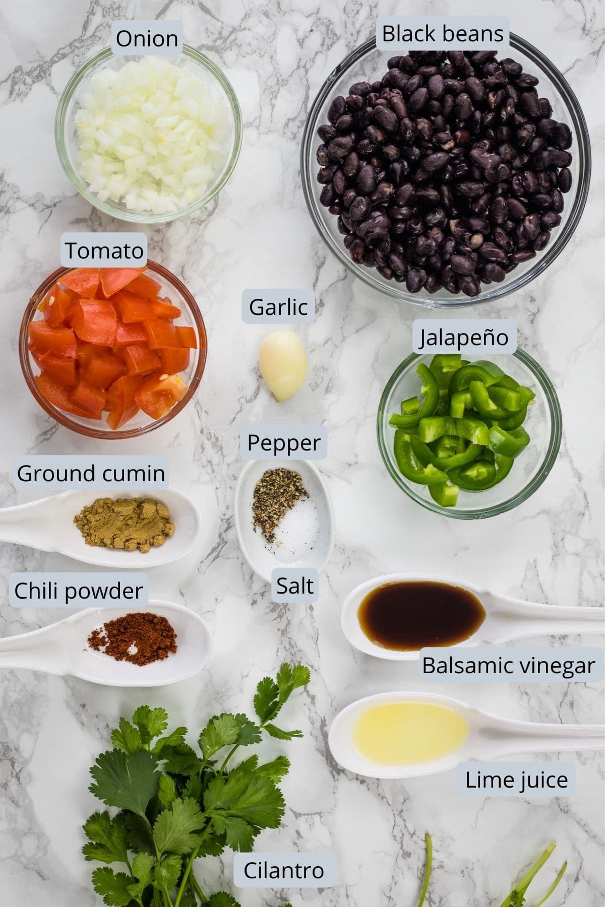 Ingredients used in black bean dip in individual bowls on marble surface.