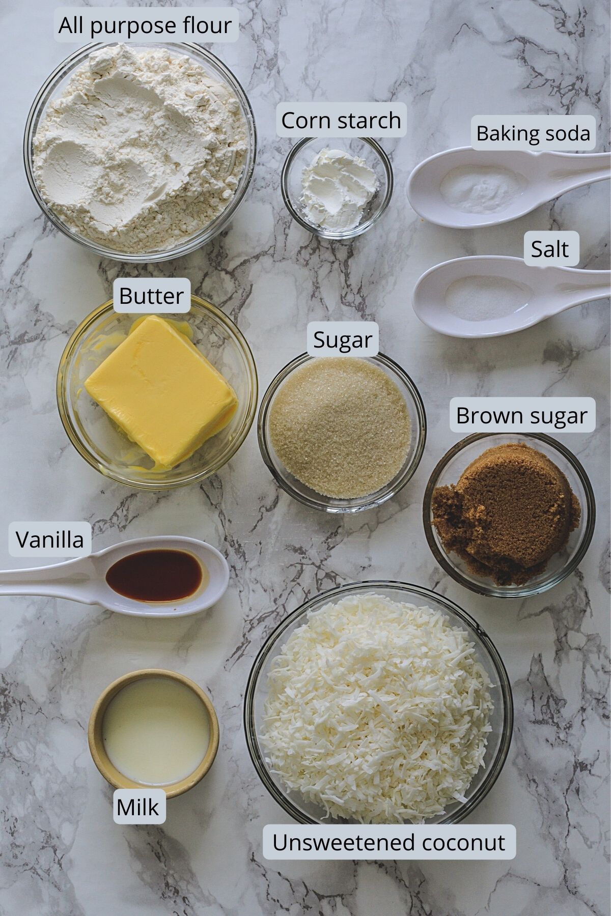 Ingredients used in eggless coconut cookies removed in individual bowls on marble surface.