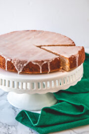 Eggless lemon cake with one slice cut on the cake stand with green napkin on side.