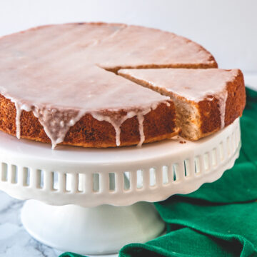 Eggless lemon cake with one slice cut on the cake stand with green napkin on side.