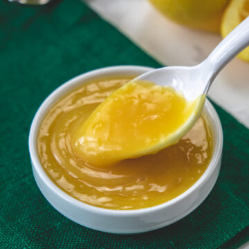 Spoonful of eggless lemon curd taking from the bowl with green napkin under the bowl.